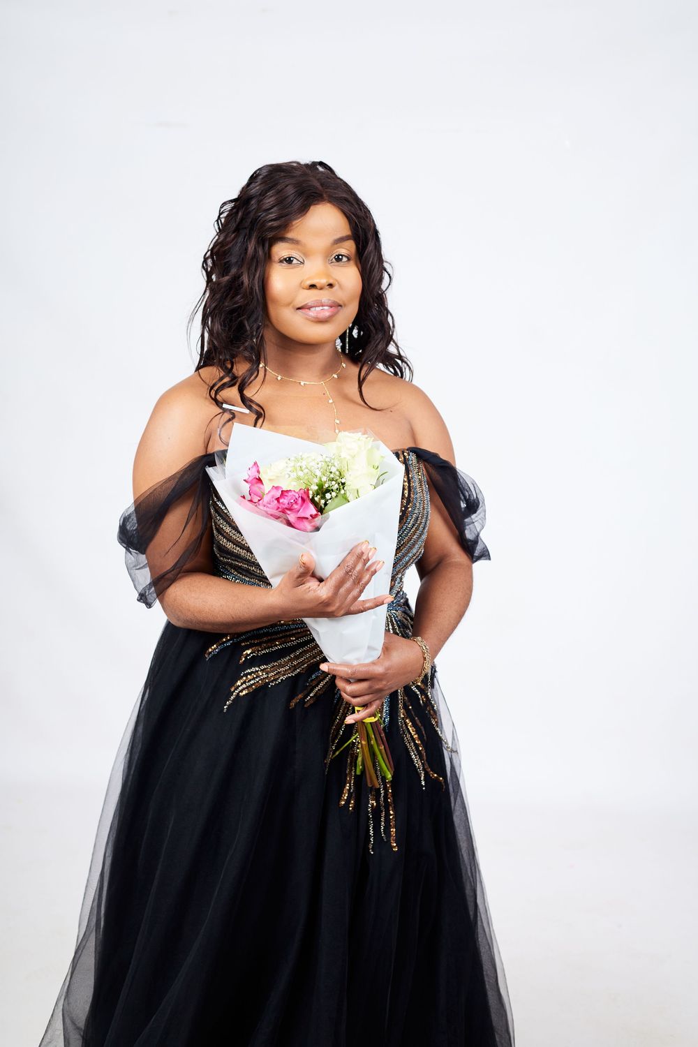 Elegant portrait in a black tulle gown holding a bouquet of pink and green flowers.