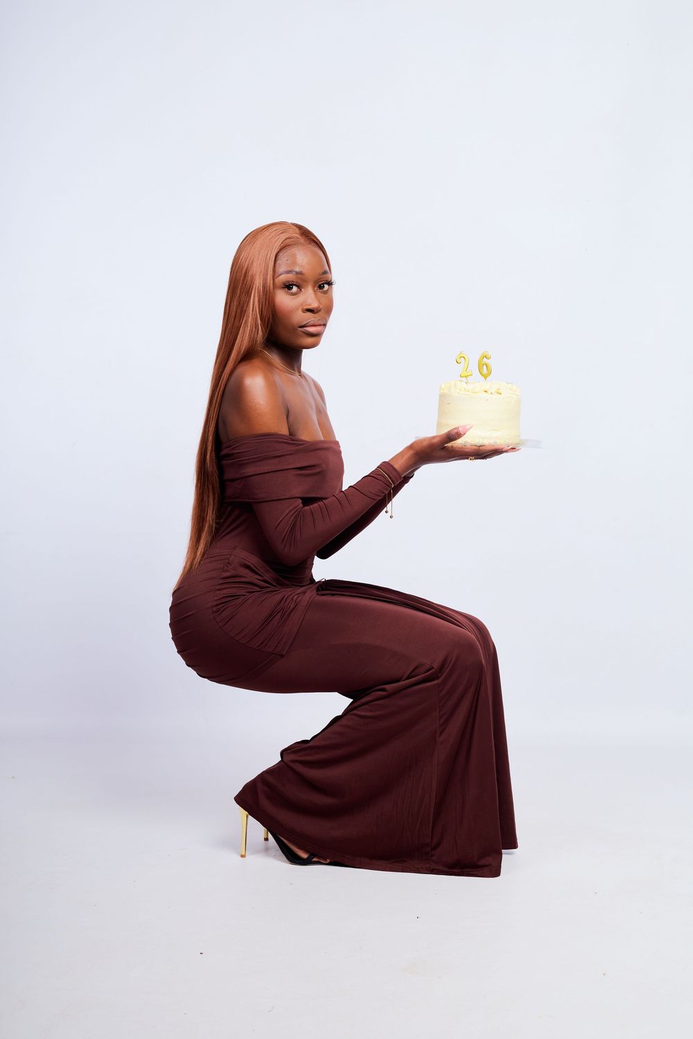 Artistic photo series in brown off-shoulder dress holding a small cake with candles.