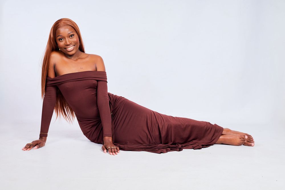 Relaxed poses in a chocolate brown off-shoulder maxi dress on white backdrop.