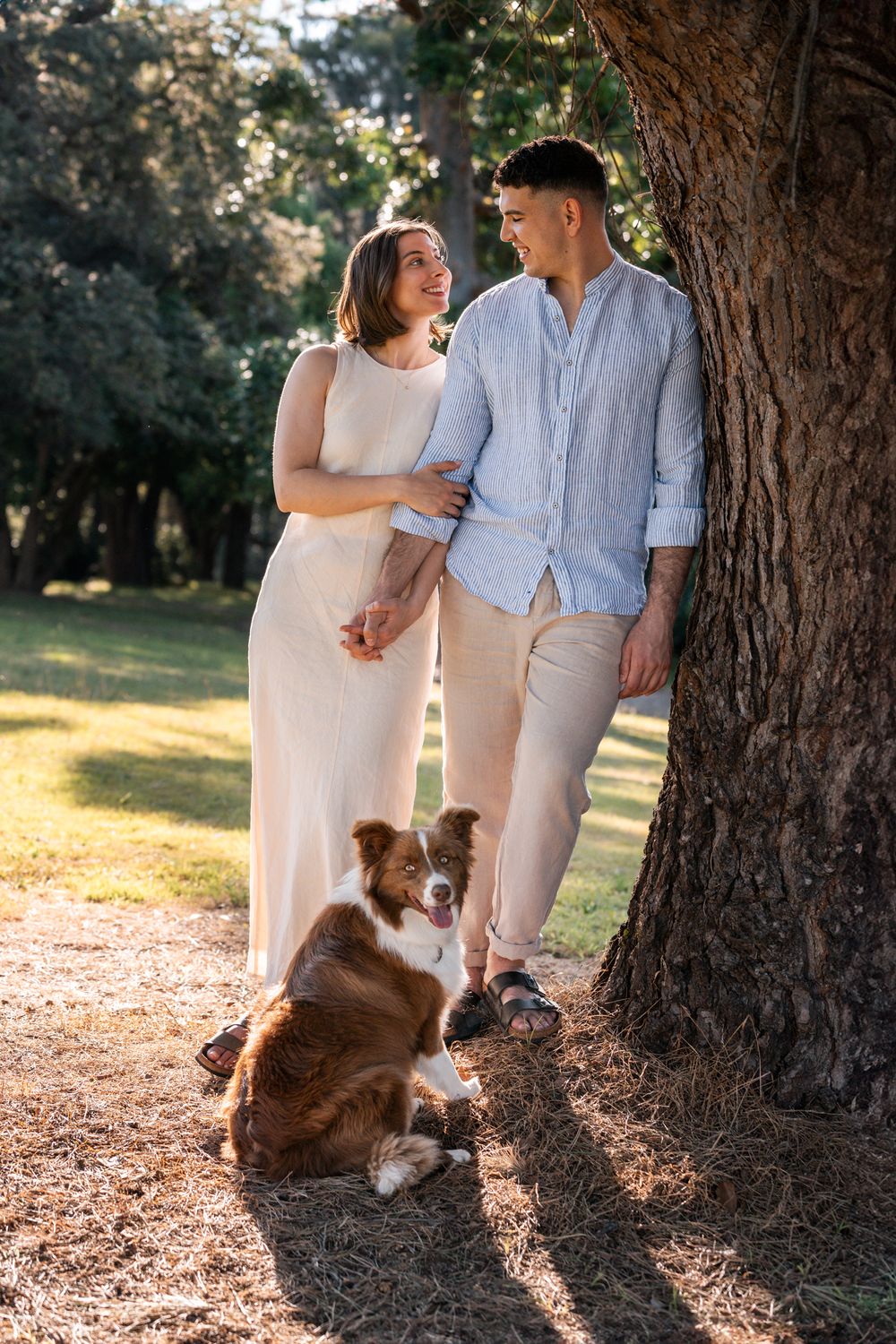 couple looks at each other while leaning towards a tree together with their dog in sydney