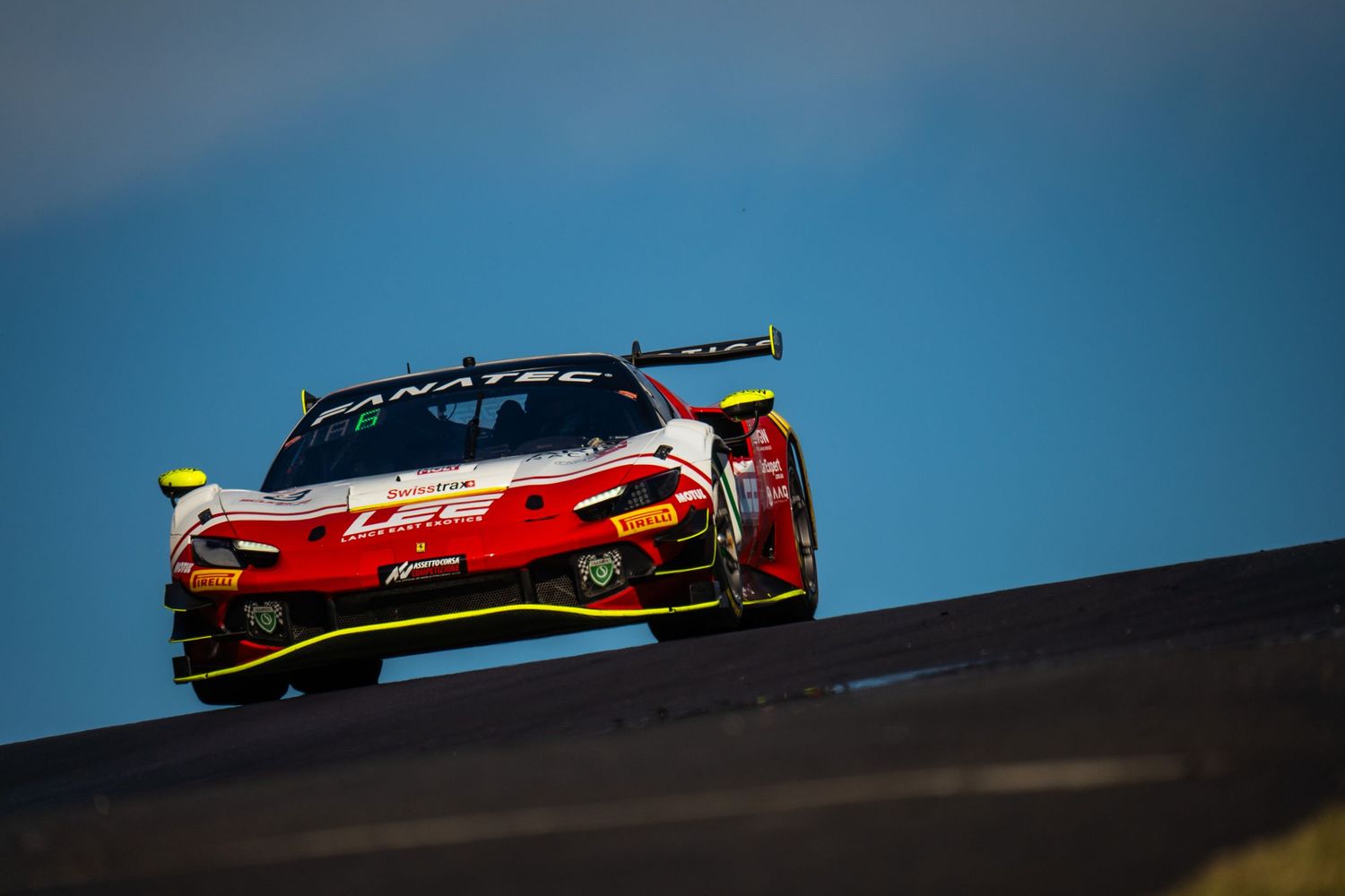 Red race car crests a hill against blue sky during competitive motorsport event.