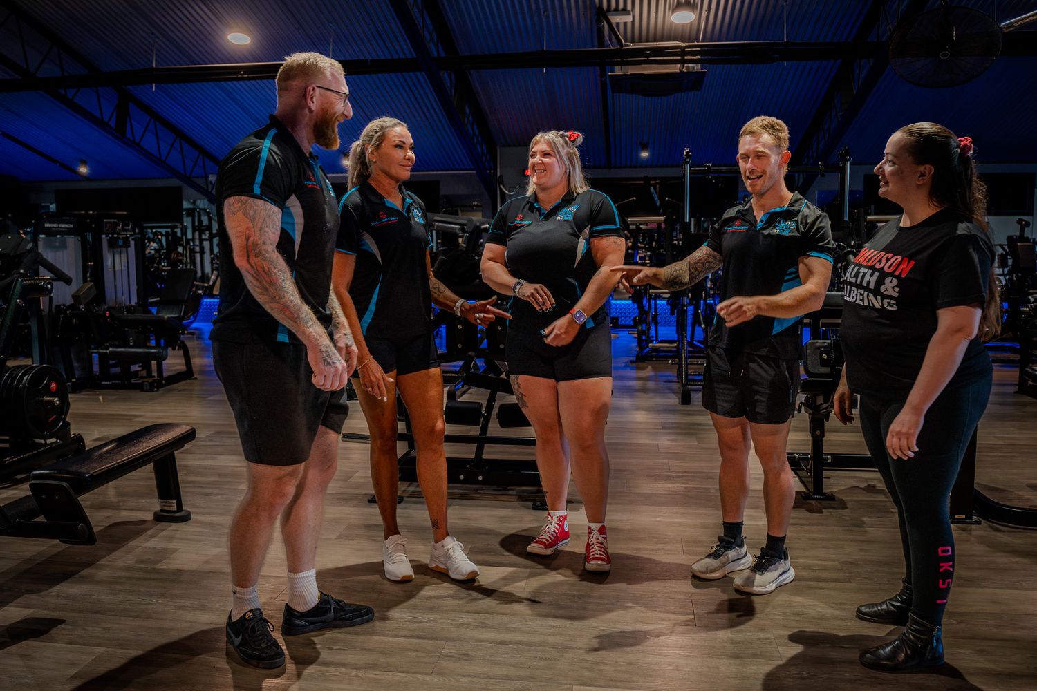 A group of fitness trainers huddle together in a gym having a discussion during evening hours.