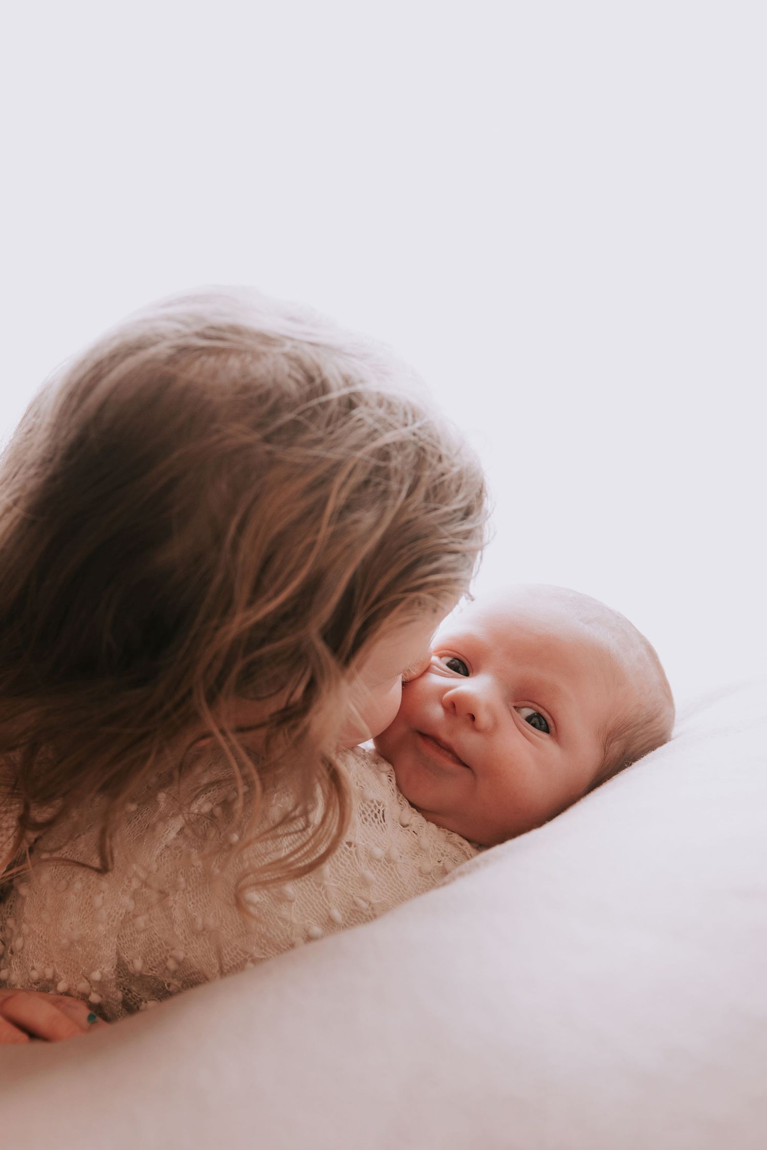 Older sibling gently kissing newborn baby during a natural light studio photoshoot in Basildon, Essex