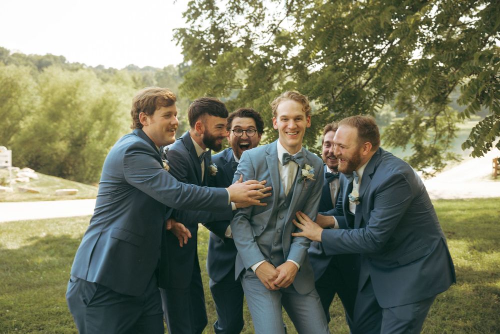 Groomsmen in blue suits laughing and celebrating together outdoors.