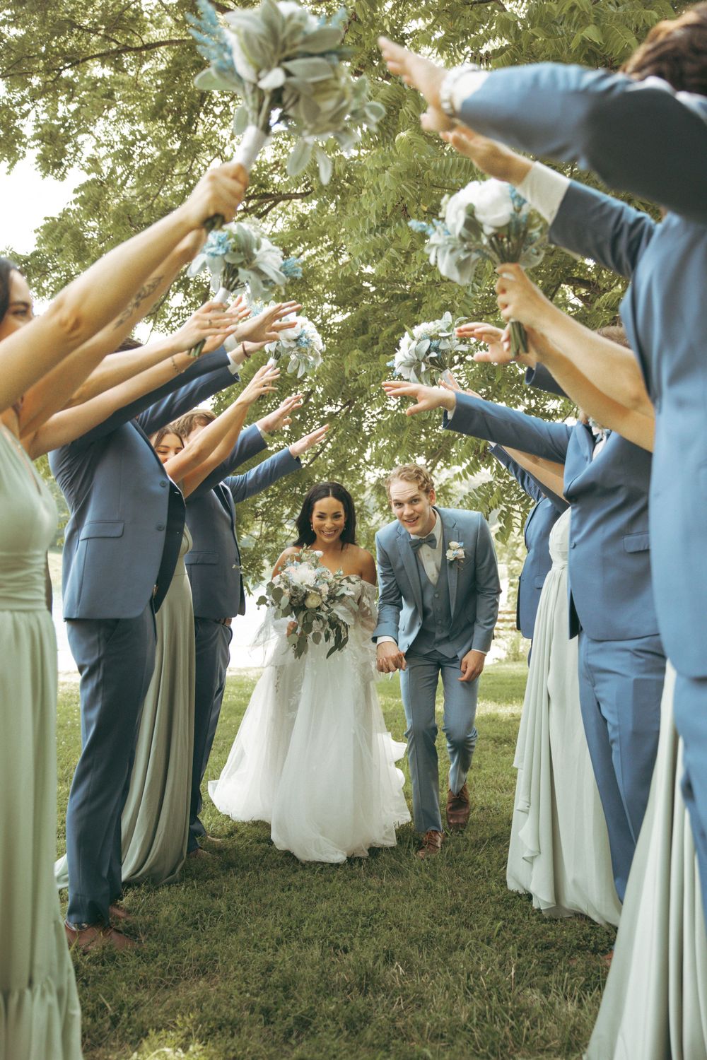 Wedding party forms tunnel with raised arms as newlyweds walk through celebratory arch.