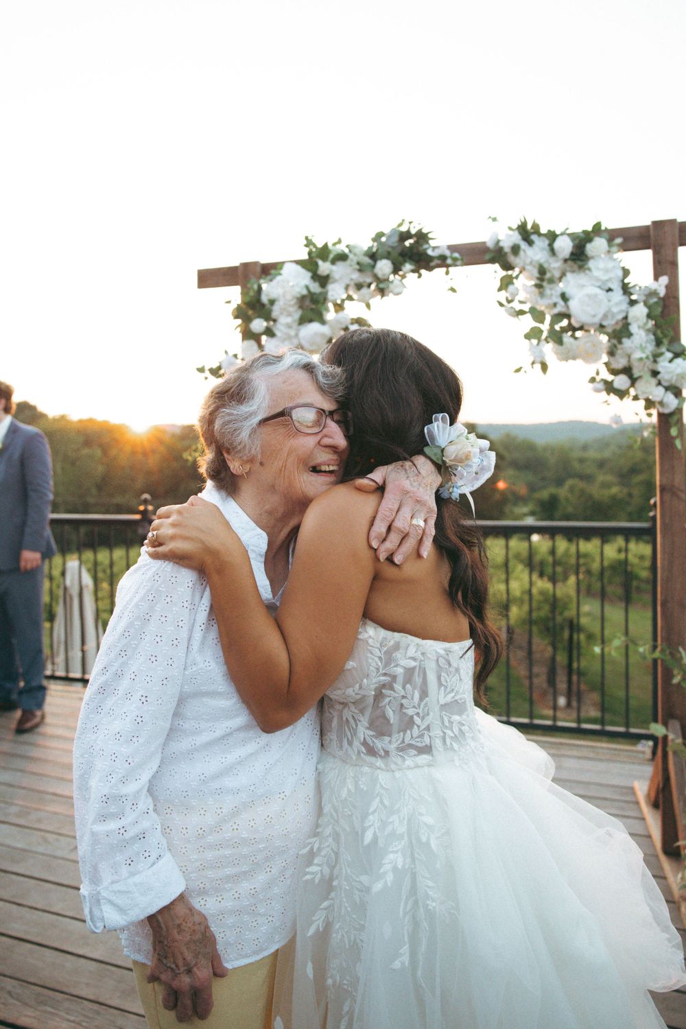 Emotional embrace shared during outdoor wedding ceremony under floral arch at sunset.