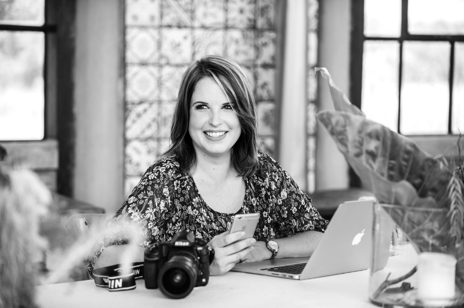 A black and white portrait of the owner, Rynali Wessels, smiling, surrounded by her camera.