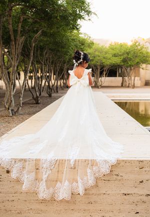 Bride in a stunning white ball gown with lace cathedral train and bow back, standing on a stone path outdoors.