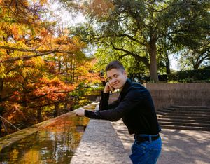 A photographer takes photos of vibrant autumn foliage along a stone pathway in a scenic park setting. Senior session downtown fort worth