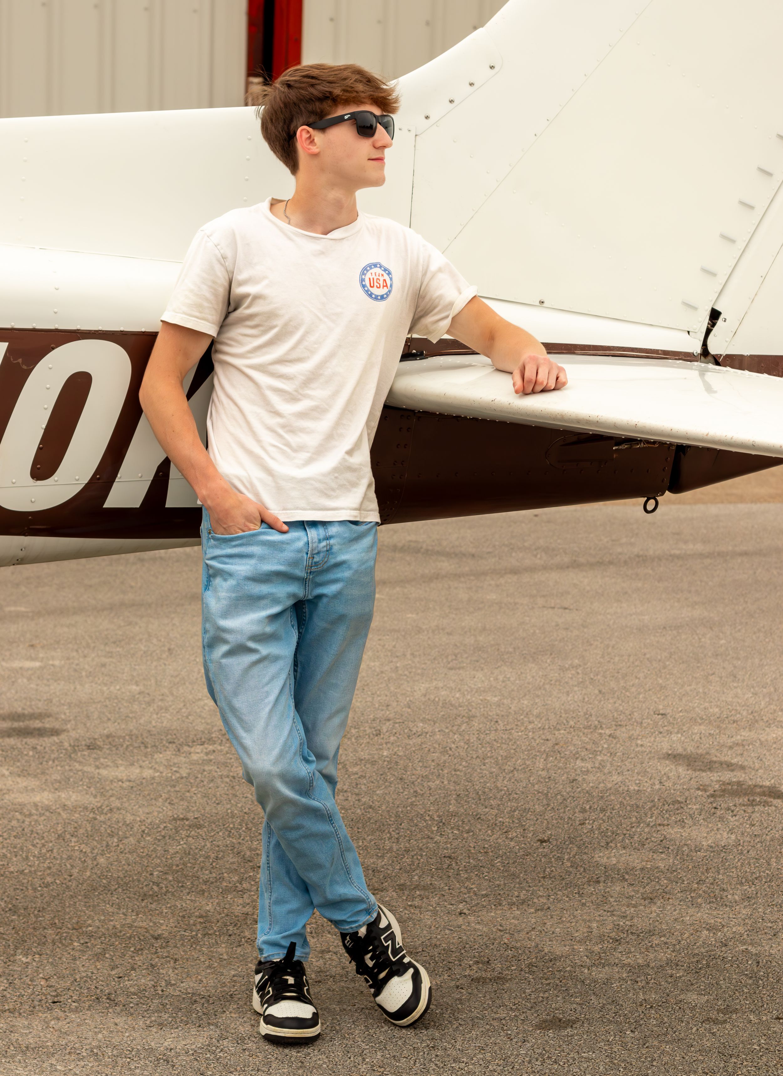 A child in jeans and white t-shirt walking on concrete near an aircraft. Senior session with airplane. Fort Worth Texas photographer. Dallas