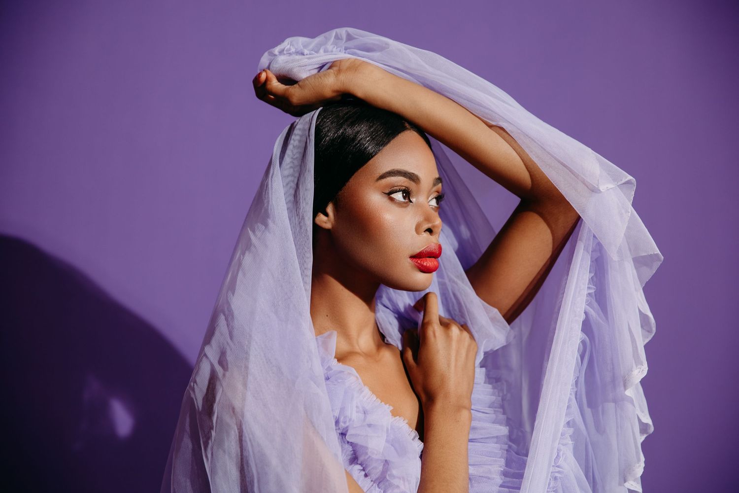Artistic portrait of a model in purple lighting wearing a flowing veil in dramatic pose.
