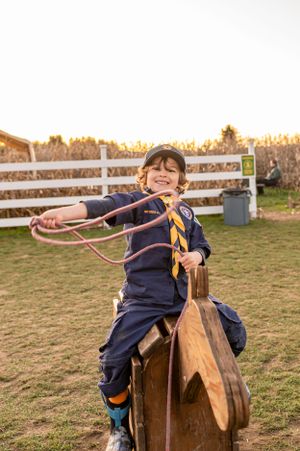 Scout on wooden horse practices rope skills at sunset near white fence.