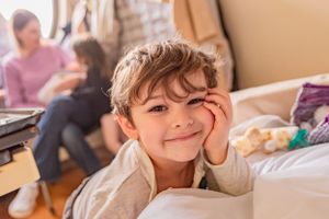 Child rests head on hand while relaxing on bed with warm natural lighting.