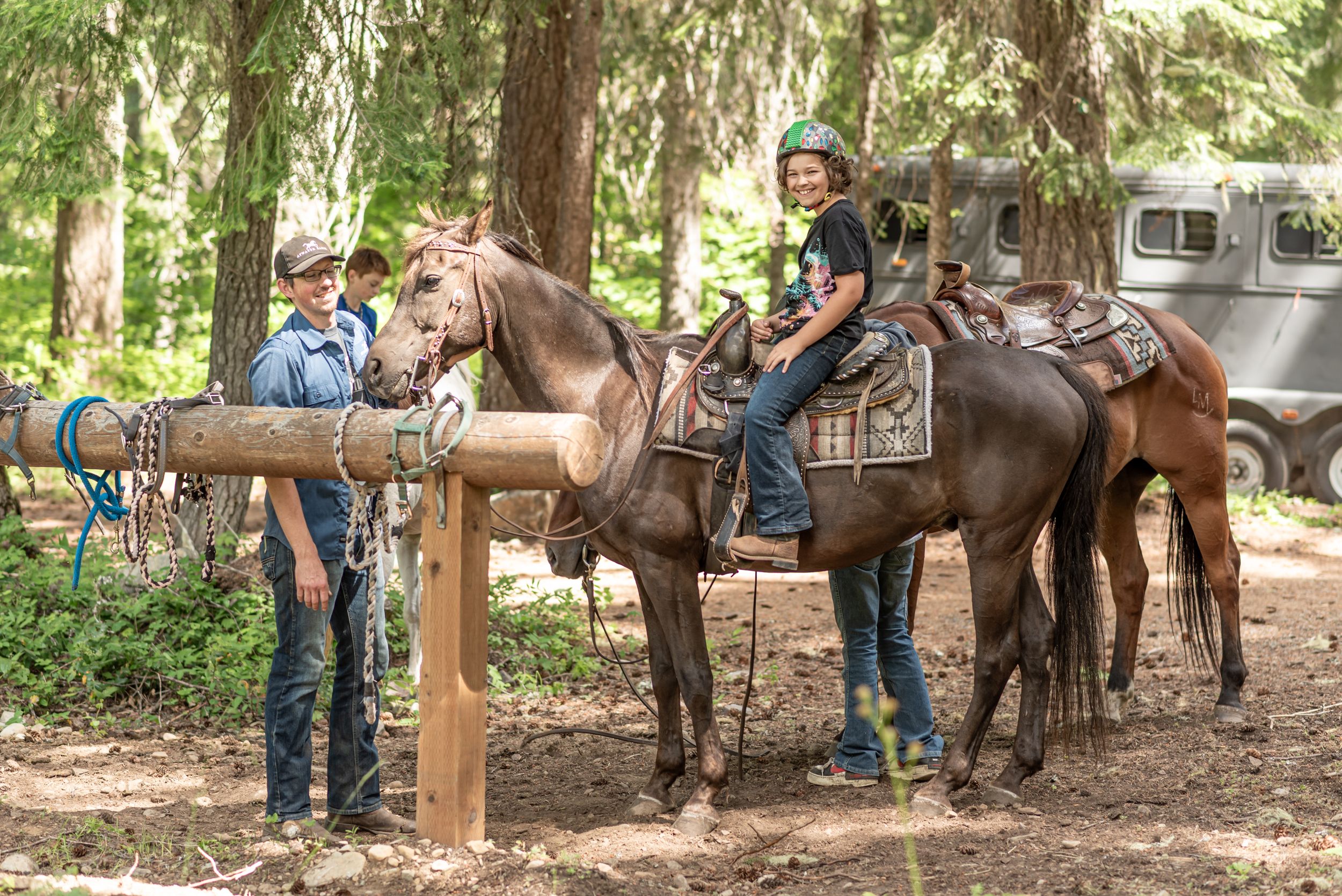 Riders on horses gather around a wooden post in a shaded forest area.