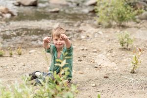 A child in a striped green shirt plays outdoors with raised hands.