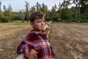 Portrait in a plaid shirt standing in an open field at golden hour.