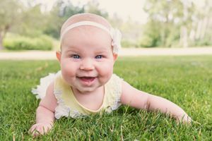 Baby in pale dress crawls on grass during springtime photo session.