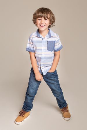 Child in striped shirt and jeans strikes fun pose against neutral backdrop.