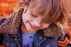Close up of child wearing brown sherpa jacket smiling warmly.