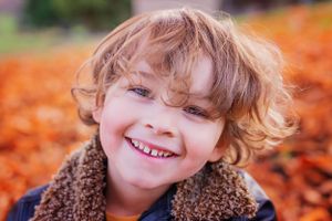 Close portrait of child with curly hair wearing sherpa collar jacket against fall leaves.