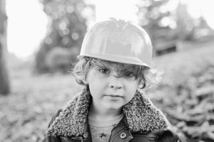 Black and white portrait of child wearing hard hat and sherpa collar jacket.