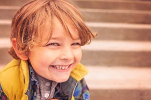 Child in yellow jacket smiles brightly against a blurred background.