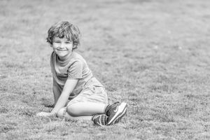 A black and white candid photo captures a playful moment sitting on grass.