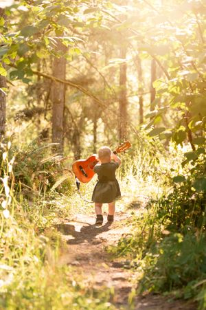 Small figure carrying guitar walks on forest path in golden sunlight.