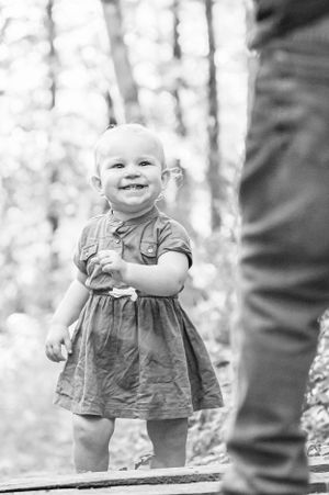 Young child in dress smiles while standing on wooden path in forest.
