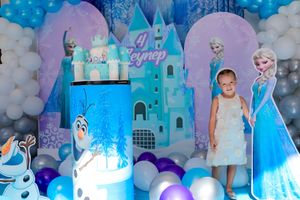 Winter-themed party display featuring a castle cake, balloon decorations, and cartoon character standees.