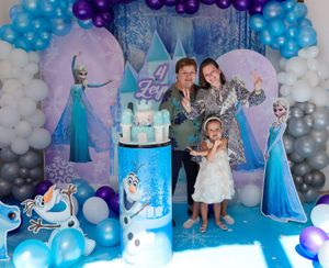 Frozen-themed birthday party setup with blue and white balloon arch and castle backdrop.