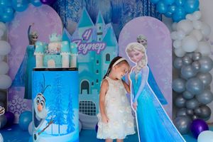 Festive Frozen-themed party backdrop with castle design and balloon decorations in blue and purple.