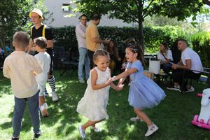 Children dancing and playing together at an outdoor party in a sunny garden setting.