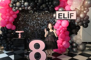 Birthday party setup with pink and black balloon arch and large number 8 decoration on checkered floor.