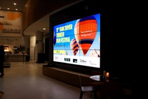Modern flat screen TV mounted on dark wall displaying a digital advertisement with blue and red graphic elements.