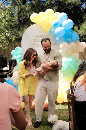 Baby celebration event with yellow and blue balloon arch backdrop in an outdoor garden setting.