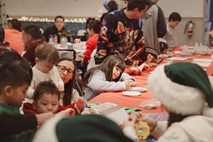 People in winter clothing gathered around long tables participating in crafts and activities at a community event.