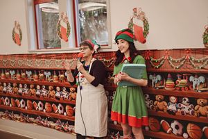 Two people in festive holiday attire stand in front of a shelf display filled with Christmas decorations and ornaments.