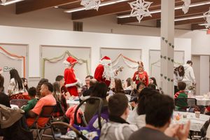 A festive holiday party scene in a community center with Santa Claus visiting as attendees gather at decorated tables.