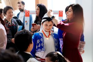 A group of people gather at an event with Turkish flags visible in the background while someone gets their hair styled.