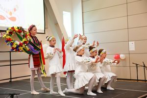 Children perform on stage wearing white dresses during a Christmas or holiday performance.