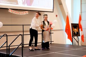 Two people stand on a stage with Polish flags and banner decorations during an indoor event presentation.