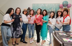 A group poses together at a party holding balloons and drinks while standing in casual dress against a light colored wall.