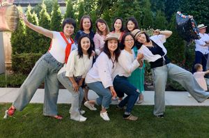 A group of people pose playfully together on a grassy lawn wearing casual clothing in an outdoor setting.