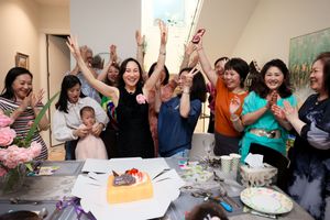 A group of people cheering and raising their hands during a celebration with cake and desserts on the table.
