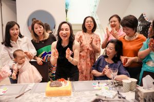 A group of friends laugh joyously while gathered around a table with a cake during a celebration.