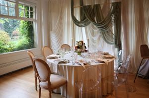 Elegant dining table setup with white linens and draped curtains in a bright room.