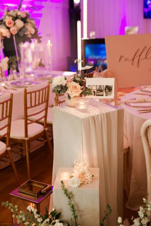 Elegant wedding table setup with white linens, peach roses, and romantic candlelight under purple lighting.