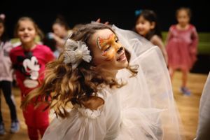 At a children's party, a dancer in white twirls energetically with a flower in her hair.