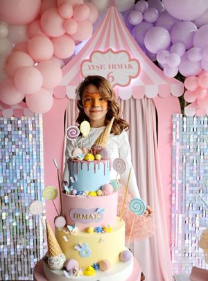 Whimsical birthday party setup with pink and purple balloons around a three-tiered pastel cake display.